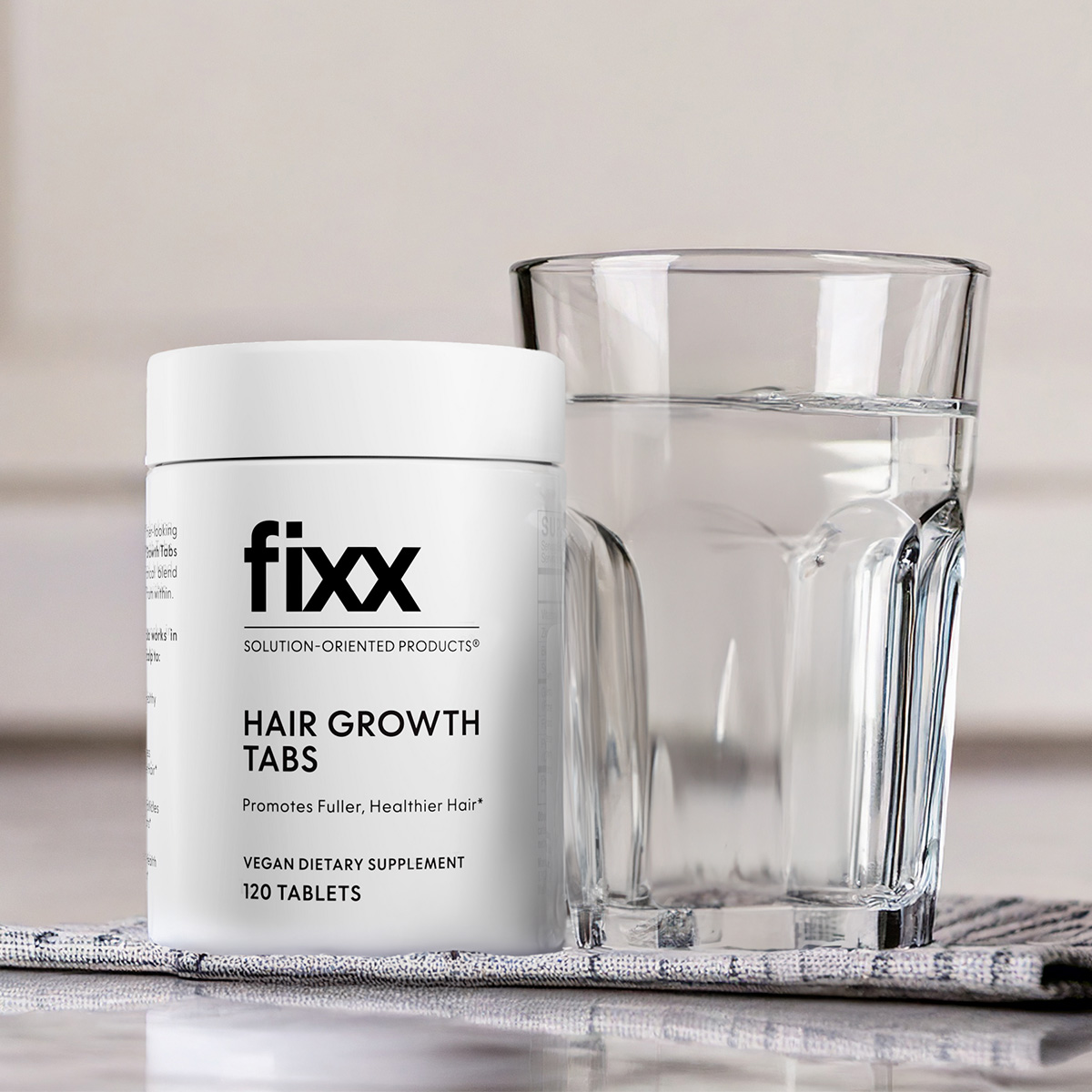 image of Fixx Hair Growth Tabs bottle beside a glass of water