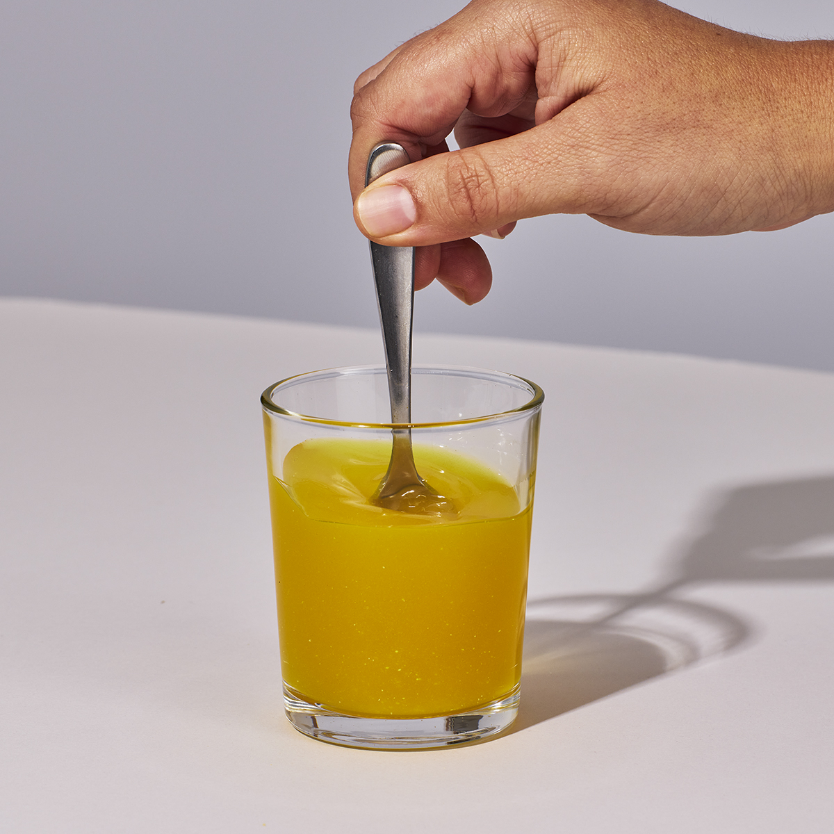 Image of someone's hand mixing up a serving of Isotonix Multivitamin Fifty Plus powder with water.