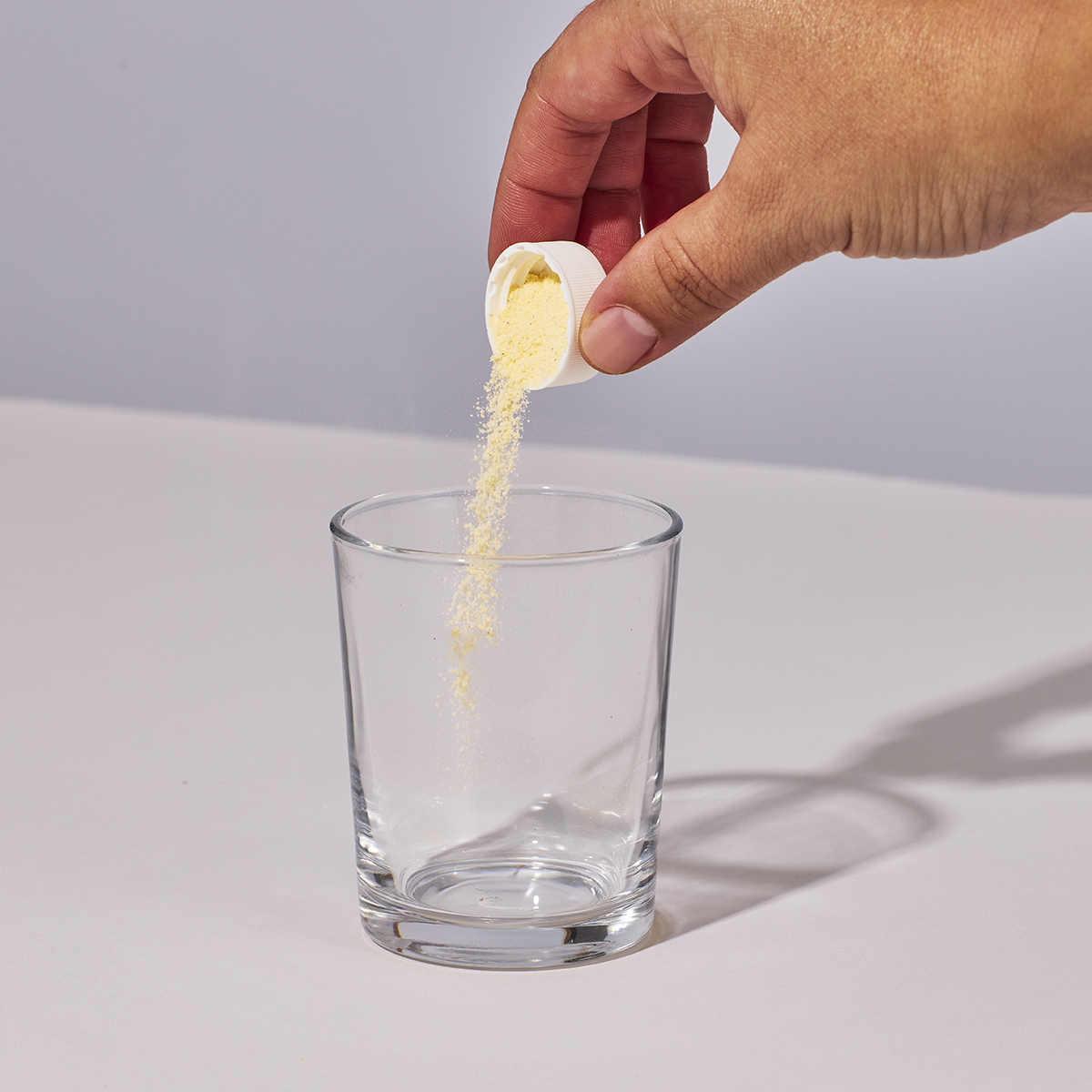 Image of someone's hand pouring a serving of Isotonix Multivitamin Fifty Plus powder into a glass.